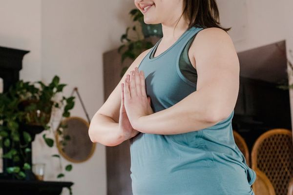 Person stretching on a mat in a brightly lit room with plants.